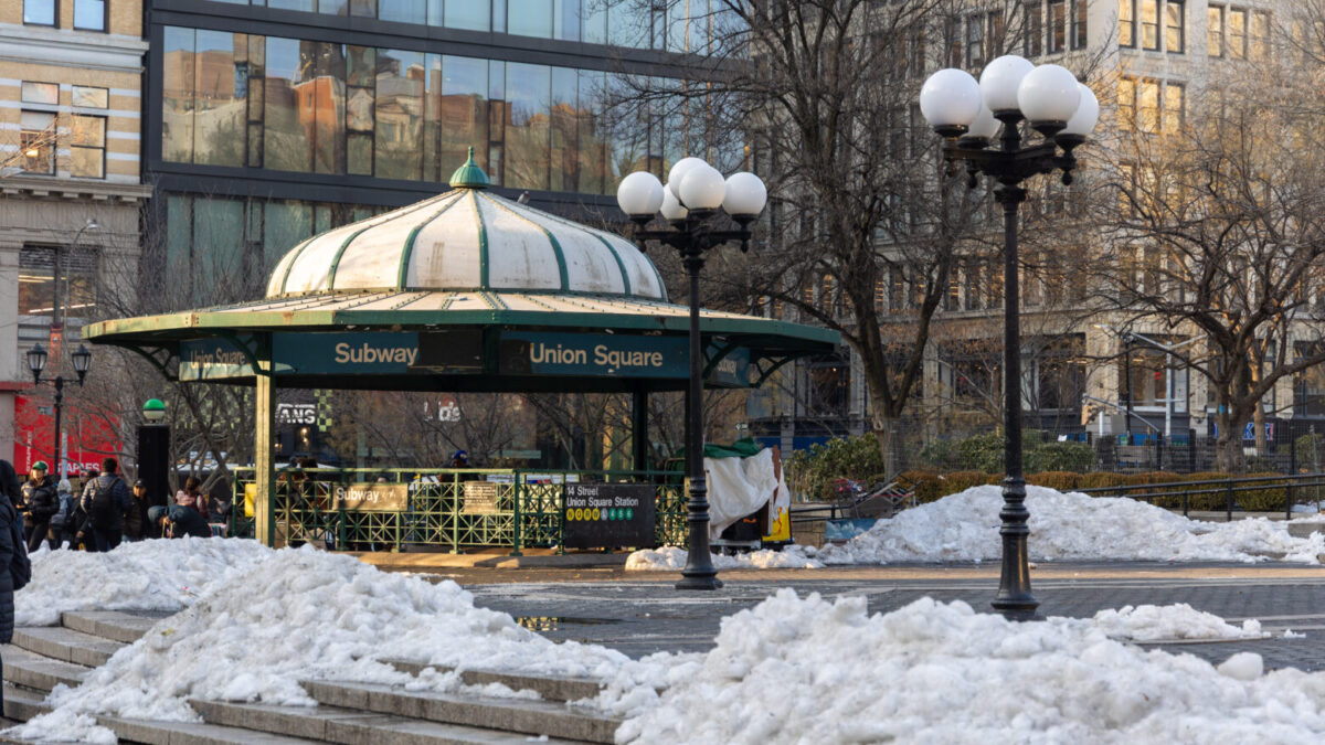 A photo of Union Square with piles of snow, the main subway entrance visible, and a crowd of people to the left.