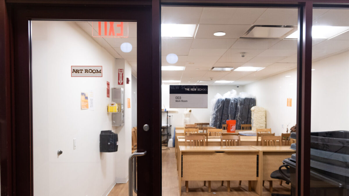 Glass entryway into a room with rows of art desks and chairs with a sign on the door that says “Art Room.”