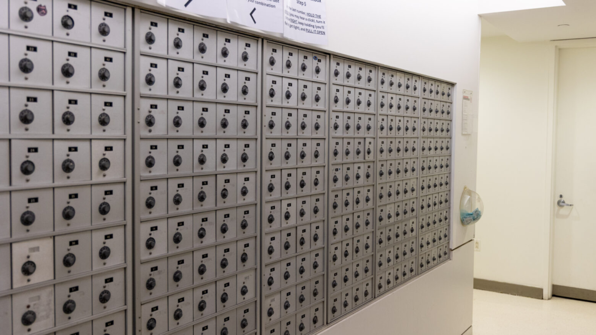 A hallway lined with small gray combination lock mailboxes.