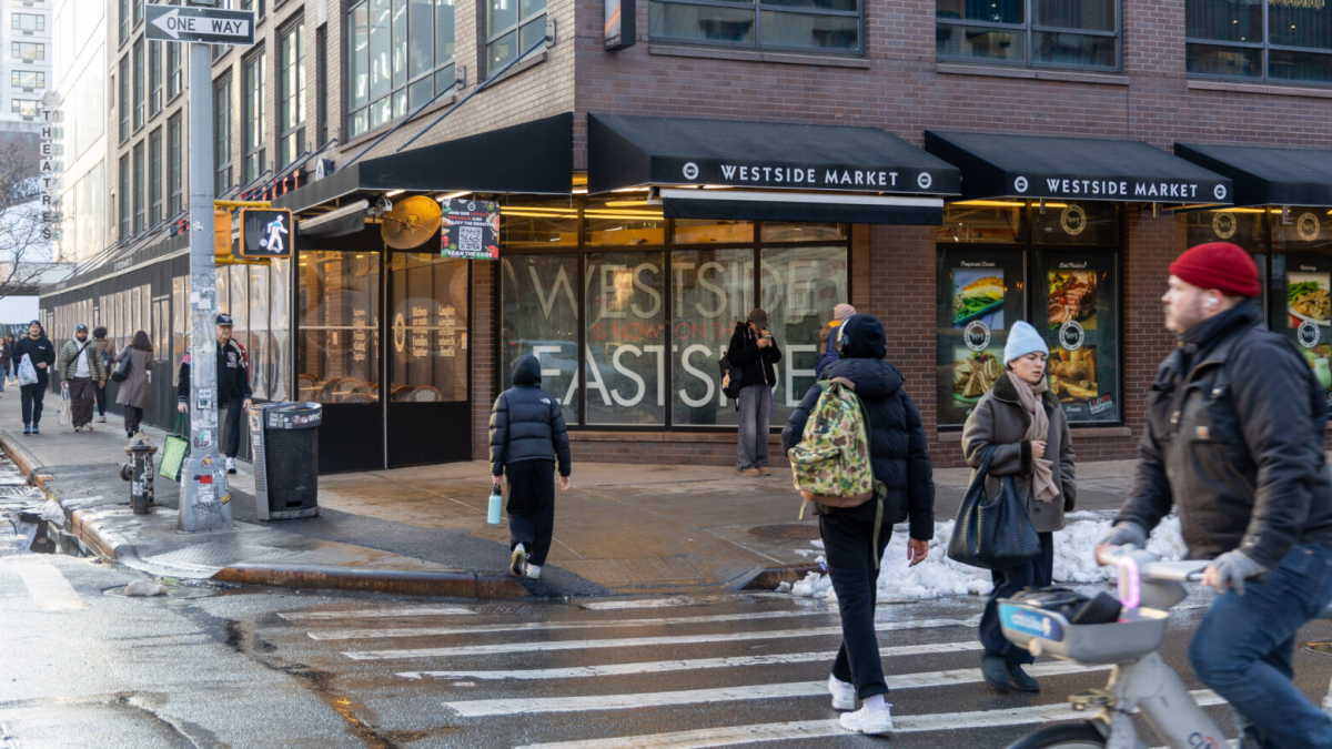 A street corner view of Westside Market covered with black awnings and a winter shelter on the left side. Through the corner window, it says, “Westside is now on the east side.”