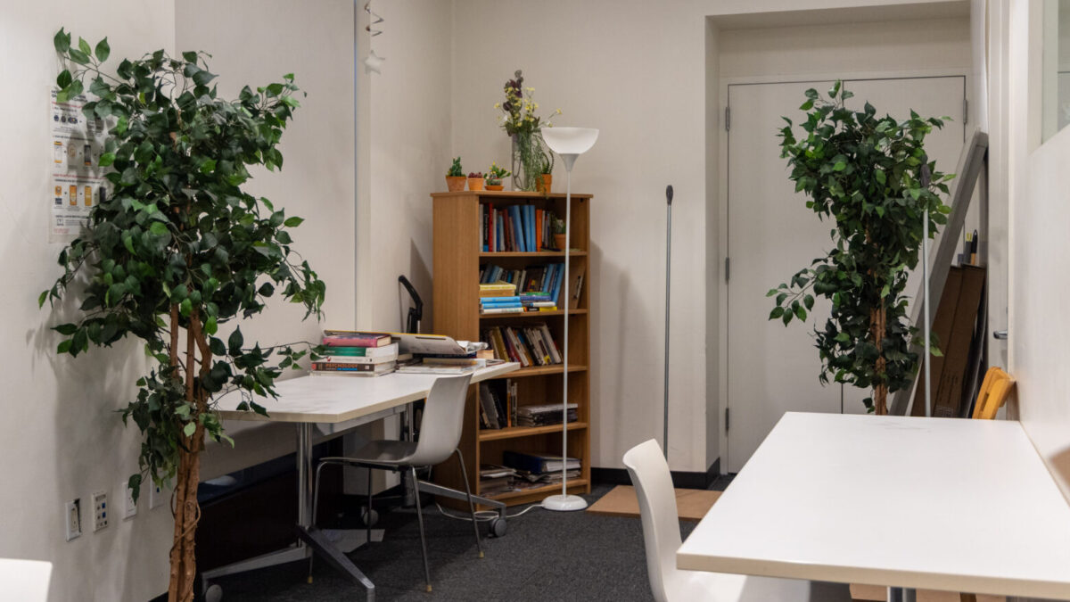 A carpeted room with potted trees, a bookshelf, and two tables and chairs.